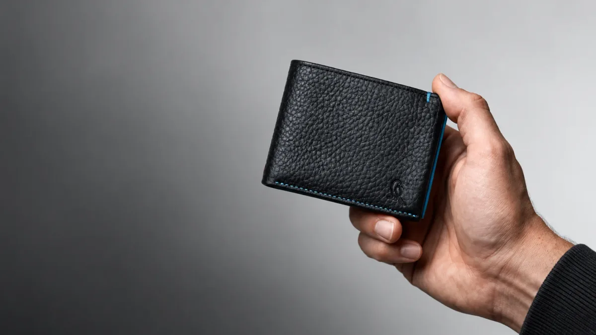 A hand holding Nirvana's black pebble-grain leather bifold wallet
